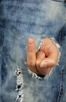 Close up man hand shows rude insulting finger gesture out of jeans rip hole