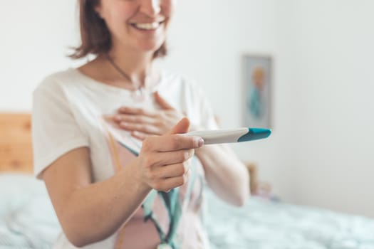 Happy mother holding pregnancy test in her hands, result is pregnant, “Schwanger”