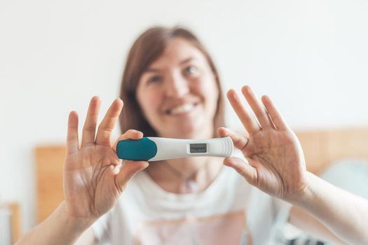 Happy mother holding pregnancy test in her hands, result is pregnant, “Pregnant”