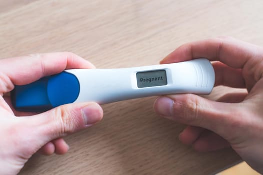 Woman hand holding pregnancy test, result is pregnant, “Pregnant”