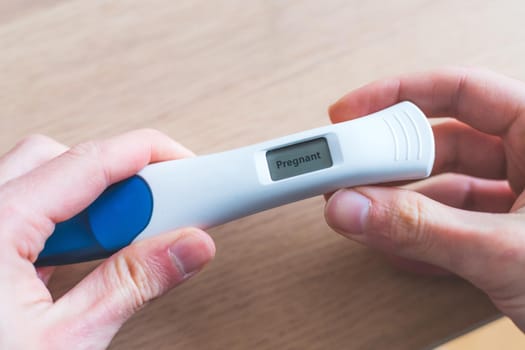 Woman hand holding pregnancy test, result is pregnant, “Pregnant”