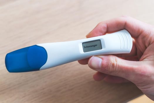 Woman hand holding pregnancy test, result is pregnant, “Schwanger”