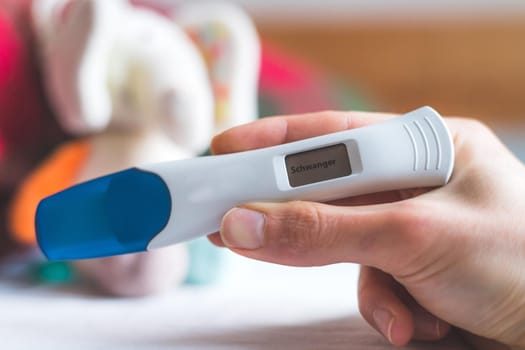 Woman hand holding pregnancy test, result is pregnant, “Schwanger”