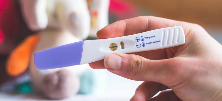 Woman hand holding pregnancy test, result is pregnant