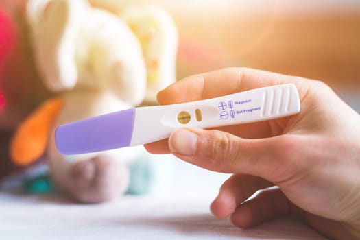 Woman hand holding pregnancy test, result is pregnant