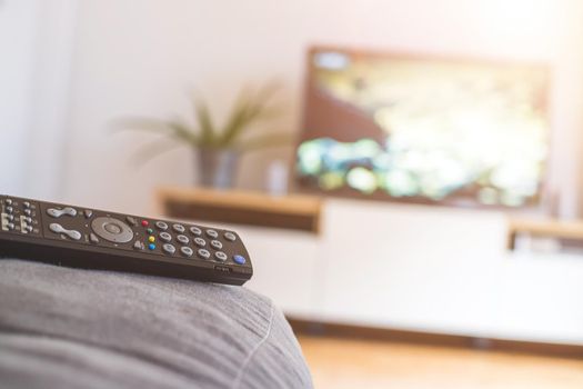 TV remote control in the foreground, tv in the blurry background. Streaming.