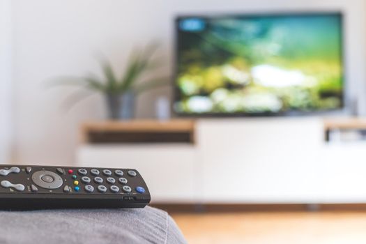TV remote control in the foreground, tv in the blurry background. Streaming.