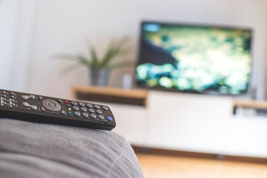 TV remote control in the foreground, tv in the blurry background. Streaming.