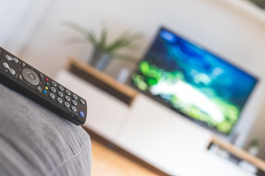 TV remote control in the foreground, tv in the blurry background. Streaming.