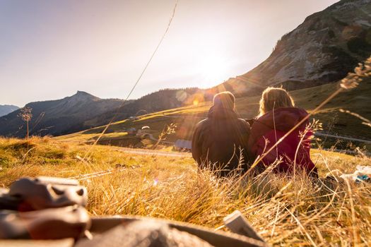 Couple in sportswear is enjoying the sunset in the mountains: sitting on the ground and enjoying the view. Alpes, Austria