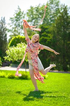 A charming girl in a light summer sundress and a pareo hat is walking in a green park. Enjoys warm sunny summer days.