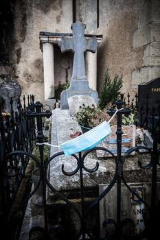 ESPELETTE, FRANCE - CIRCA JANUARY 2021: Blue surgical mask attached to the grille around a grave.