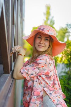 A charming girl in a light summer sundress and a pareo hat is walking in a green park. Enjoys warm sunny summer days.