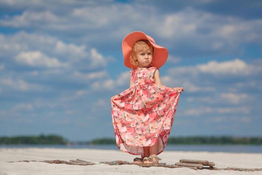 A little girl in a beautiful sarafna plays in the sand on the beach.