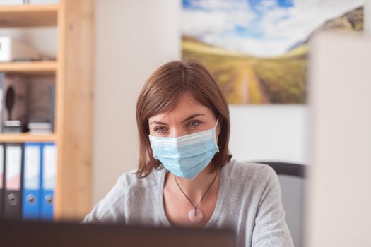 Young woman wearing face mask is working in the office during corona crisis