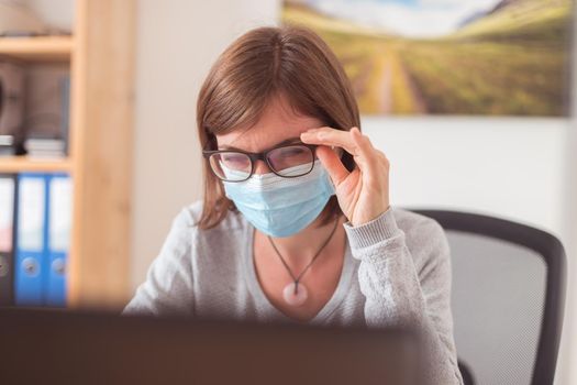 Young woman with glasses wearing face mask is working in the office during corona crisis
