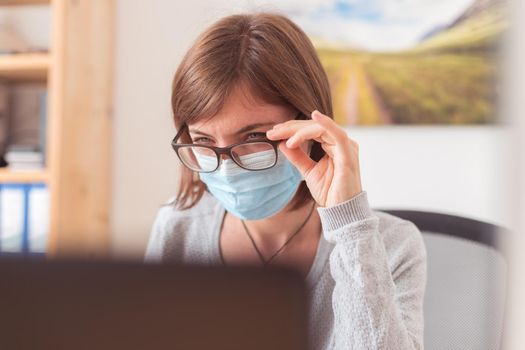 Young woman with glasses wearing face mask is working in the office during corona crisis