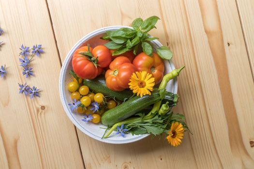 Fresh colorful vegetables in a bowl, raised in the own garden. Tomatoes, zucchini, flowers and herbs.