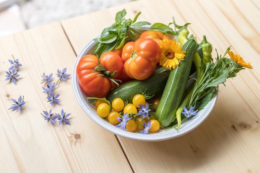 Fresh colorful vegetables in a bowl, raised in the own garden. Tomatoes, zucchini, flowers and herbs.