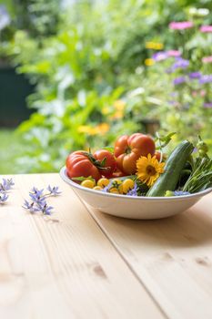 Fresh colorful vegetables in a bowl, raised in the own garden. Tomatoes, zucchini, flowers and herbs.