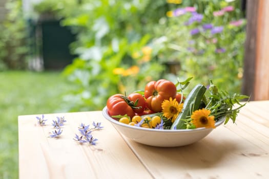 Fresh colorful vegetables in a bowl, raised in the own garden. Tomatoes, zucchini, flowers and herbs.