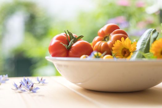 Fresh colorful vegetables in a bowl, raised in the own garden. Tomatoes, zucchini, flowers and herbs.