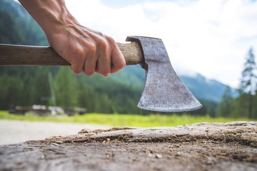 Close up of old male hand holding axe attached to a tree trunk, countryside