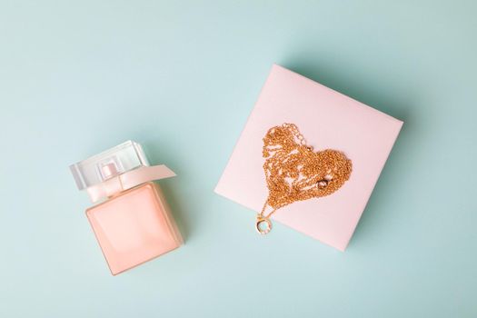 A gift for Valentine's Day. Perfume and a box with a gold chain on a blue background. Chain in the shape of a heart.