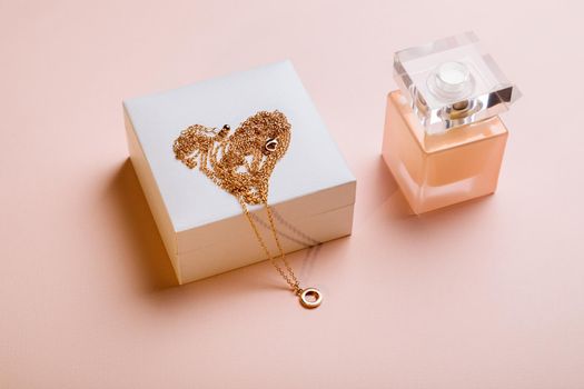 A gift for Valentine's Day. Perfume and a box with a gold chain on a pink background.