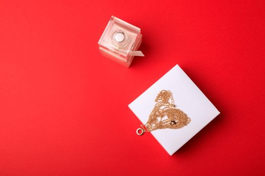 A gift for Valentine's Day. Perfume and a box with a gold chain on a red background.