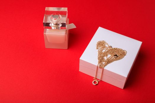 A gift for Valentine's Day. Perfume and a box with a gold chain on a red background.