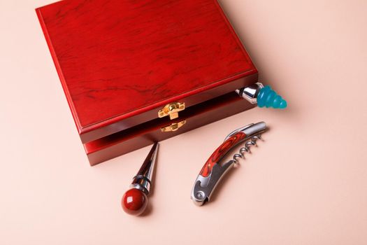 Gift set of corkscrew and removable lids. Wine corks and bottle openers in a wooden box on a pink background.