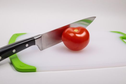 A fresh red tomato and a large chef's knife lie on a cutting board. On an isolated white background.