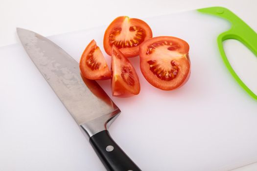 On a cutting board is a fresh red cut tomato and a large chef's knife. On an isolated white background.