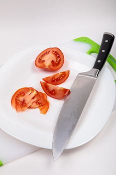 On a cutting board is a fresh red cut tomato and a large chef's knife. On an isolated white background.