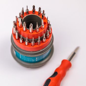 A set of working tools with a screwdriver and bits for repair, in an open plastic box with iron bits, inside a screwdriver.