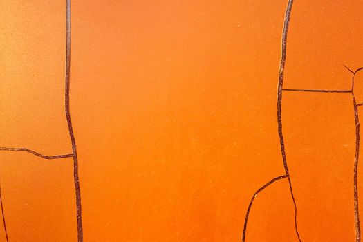 Cracked orange paint on the wall. The texture has peeled off under the influence of atmospheric influences. Background with large cracks.