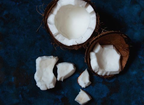 Open coconut lies on a dark blue background next to broken pieces lying randomly