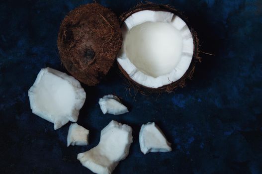 Open coconut lies on a dark blue background next to broken pieces lying randomly