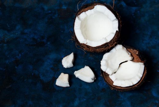 Open coconut lies on a dark blue background next to broken pieces lying randomly