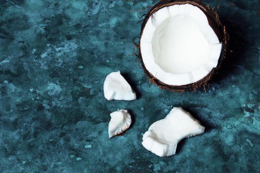 Open coconut lies on a dark blue background next to broken pieces lying randomly