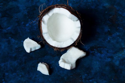 Open coconut lies on a dark blue background next to broken pieces lying randomly