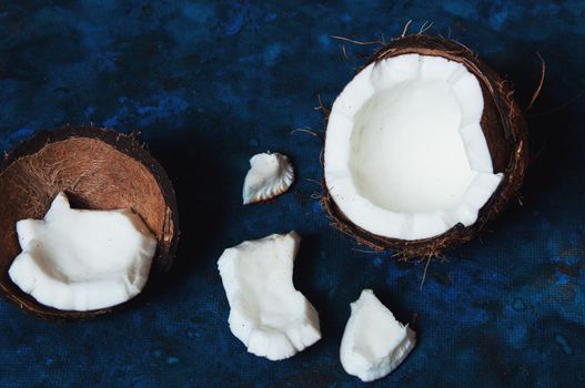 Open coconut lies on a dark blue background next to broken pieces lying randomly