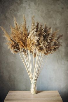 bouquet of dried flowers in brown tones stands on a wooden table in a room near a concrete wall in a loft style