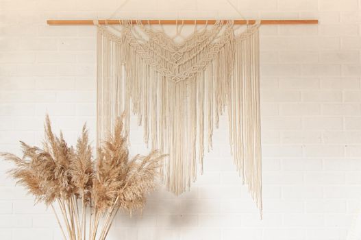 Beige reed against a white wall with a macrame wall panel. A minimal, stylish, trendy concept with a beautiful background with light neutral colors.