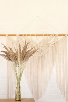 Beige reed against a white wall with a macrame wall panel. A minimal, stylish, trendy concept with a beautiful background with light neutral colors.