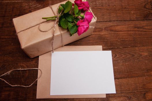gift made of craft paper, next to a bouquet of rose flowers, which lies on a wooden table