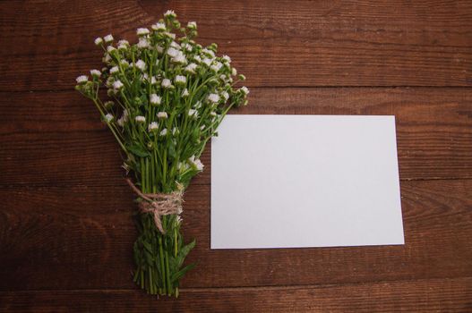 envelope made of craft paper, next to a bouquet of chamomile flowers, which lies on a wooden table