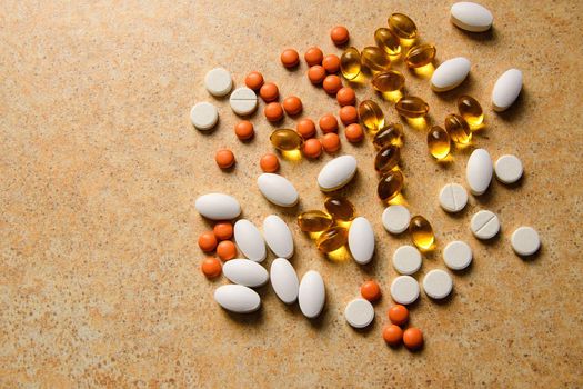 orange pills, vitamin D and fish oil capsules lie randomly against a sand countertop