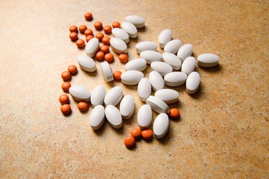 orange and white pills randomly lie on the background of sand countertops